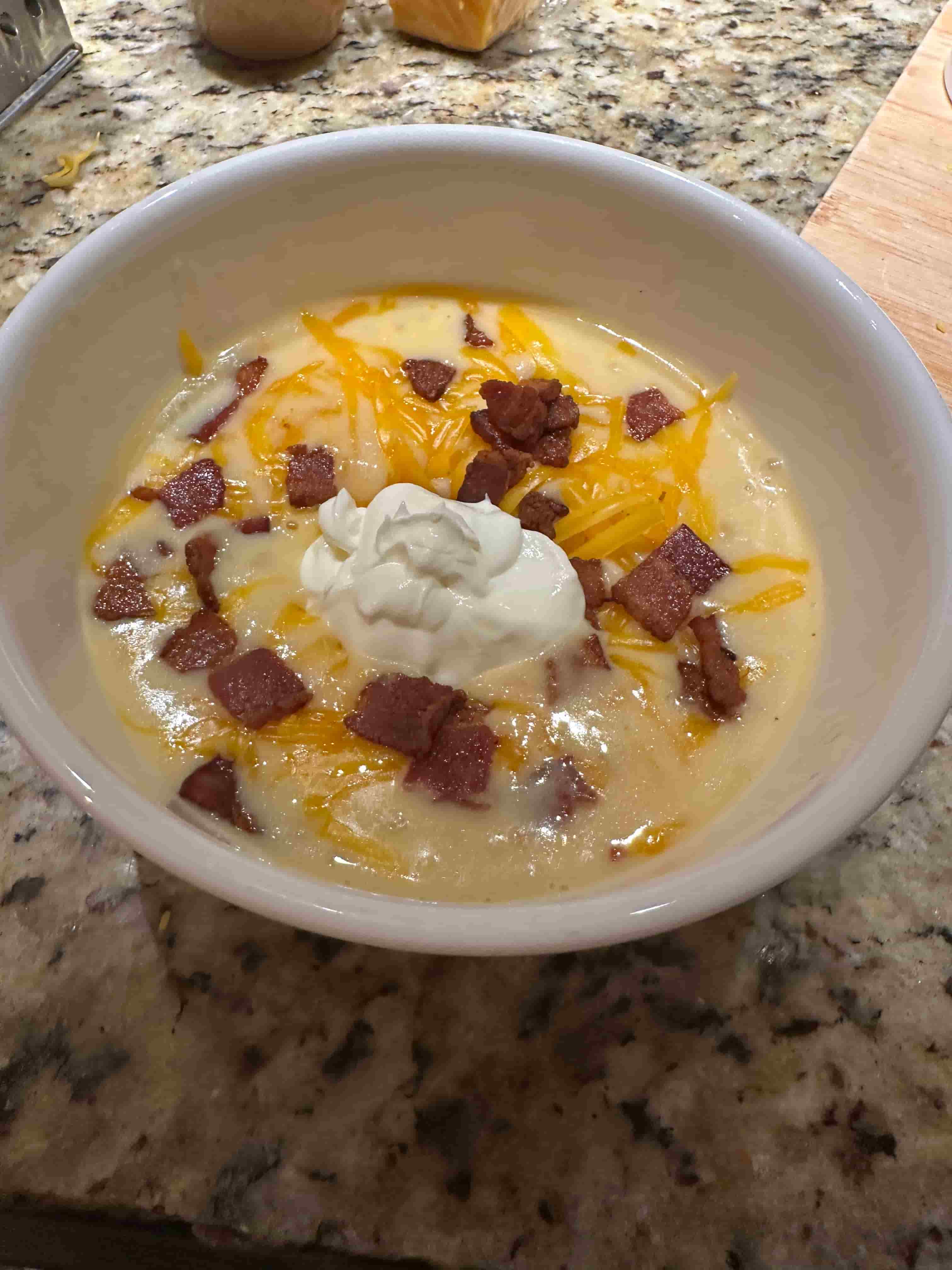 A bowl of baked potato soup with sour cream, bacon, and cheese on a counter